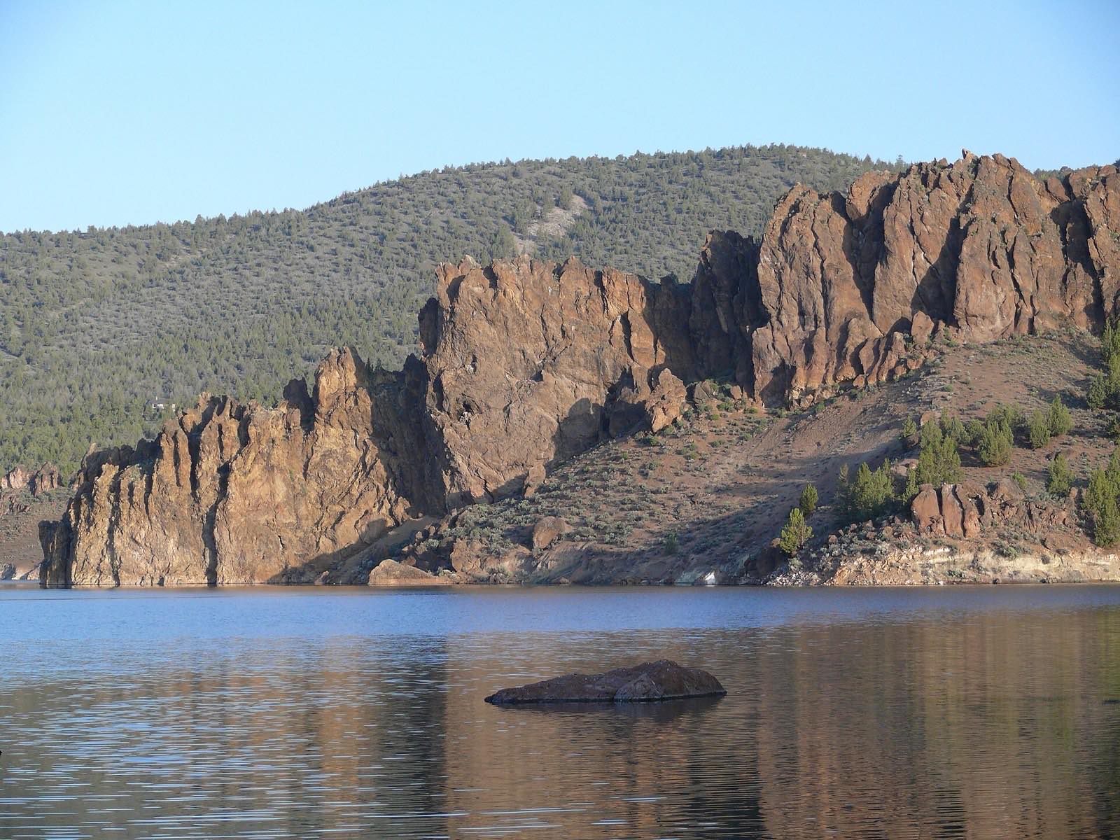 Layered basalt rimrock cliffs rising above the calm water of Prineville Reservoir near Prineville, Oregon.