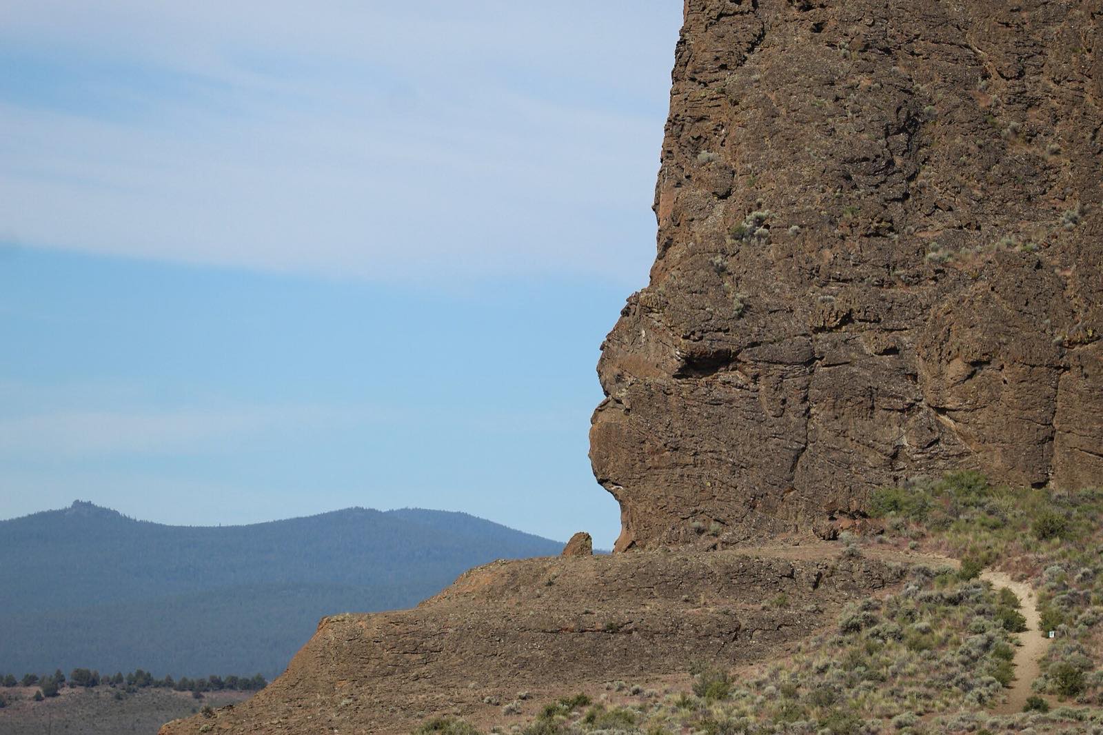 Close-up view of the eroded volcanic tuff ring at Fort Rock, Lake County, Oregon, with distant mountains under a blue sky.