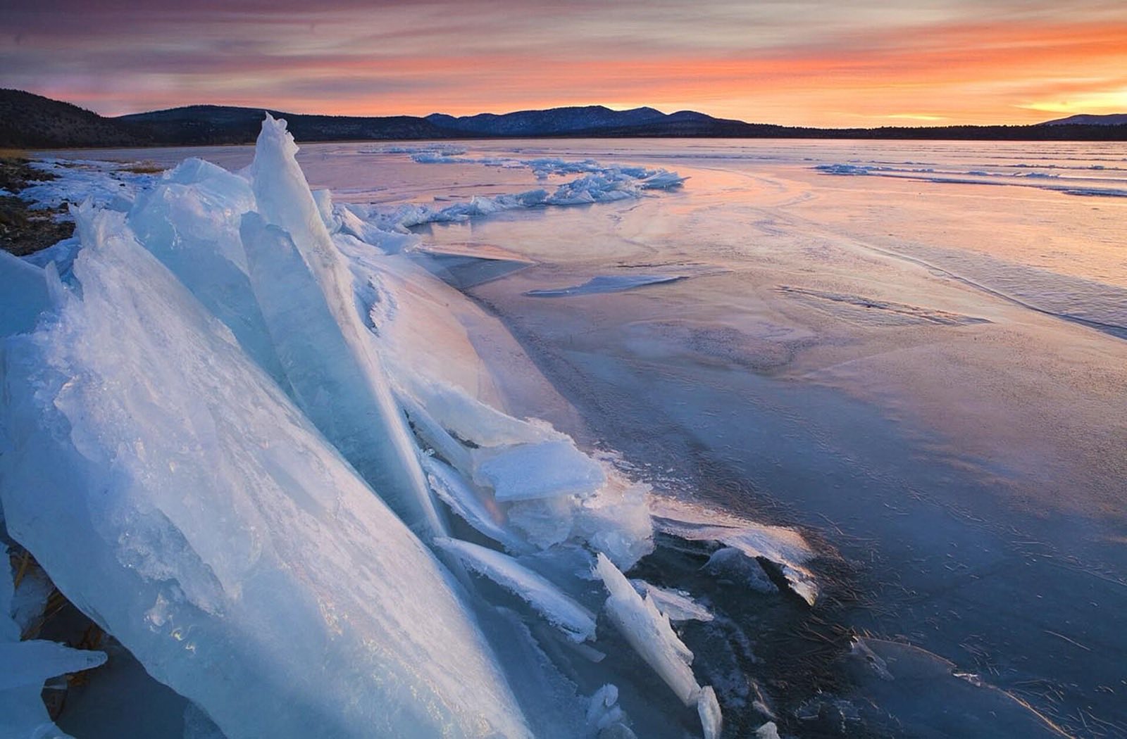 Ice formations along the shore of Eagle Lake at sunset, with mountains silhouetted on the horizon, Lassen County, California.