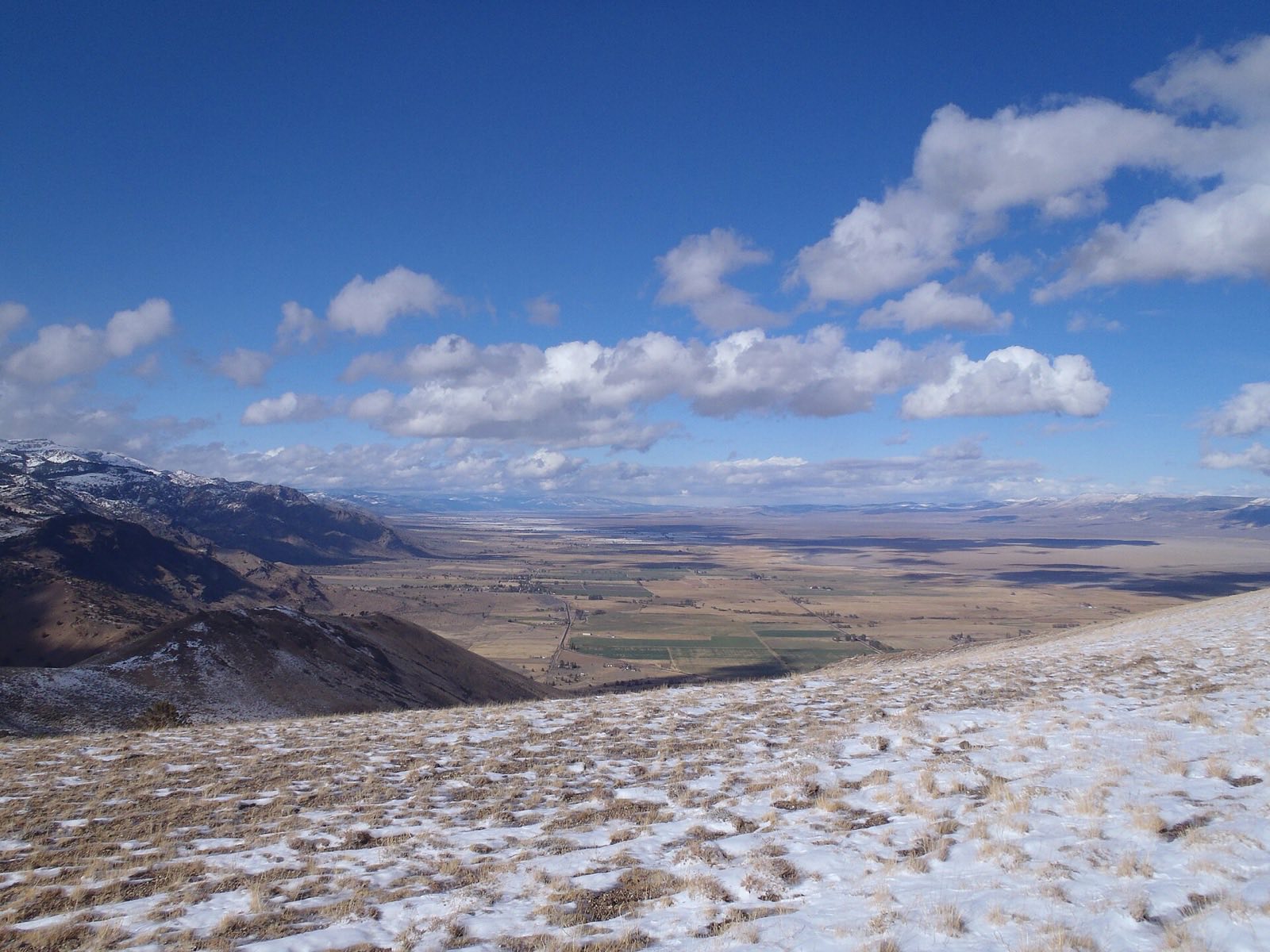 Snow-dusted ridgeline of the Warner Mountains overlooking a broad valley in Modoc County, California, under a partly cloudy sky.